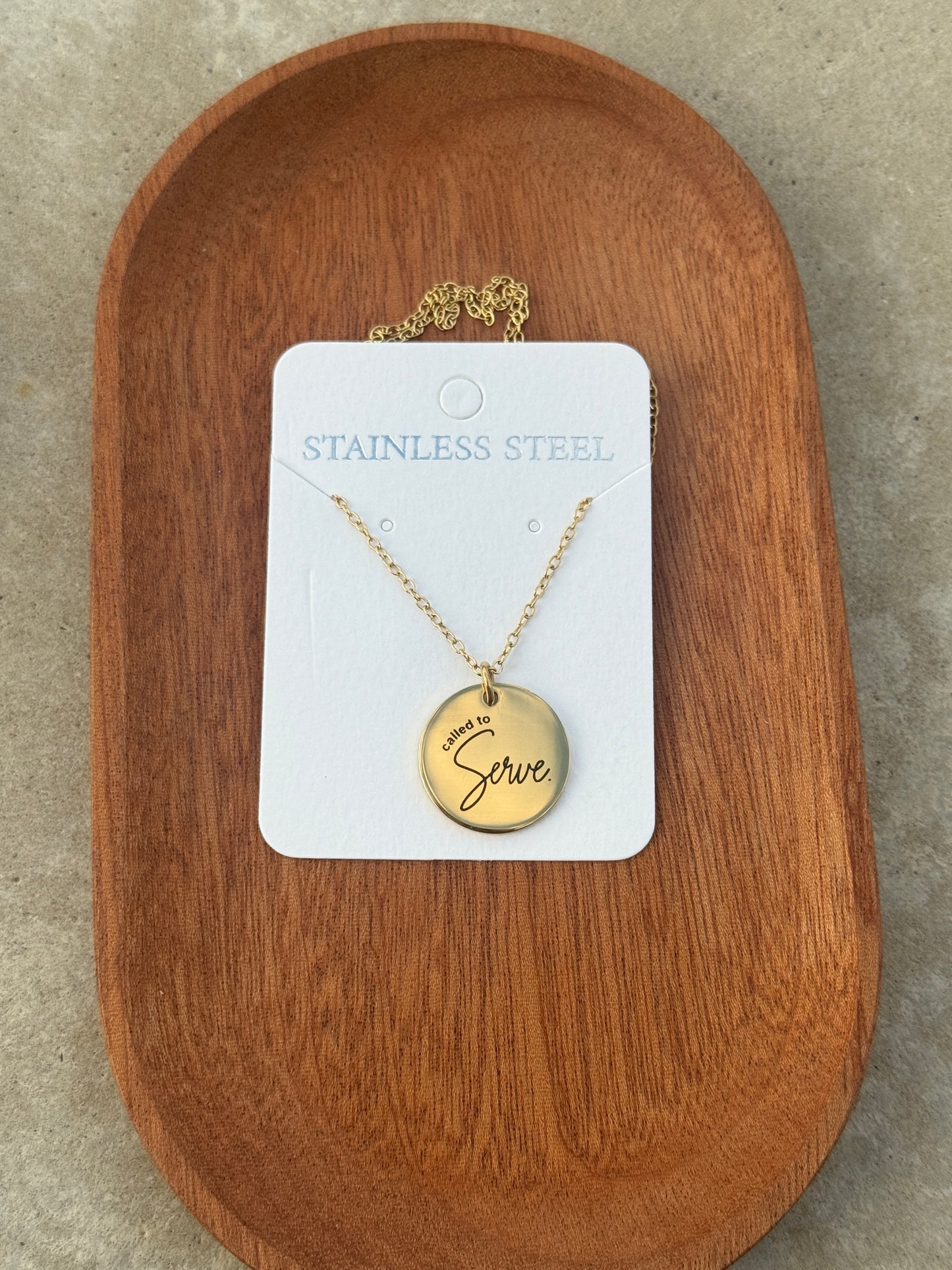 Gold necklace with a pendant on a white card, placed on a wooden surface.