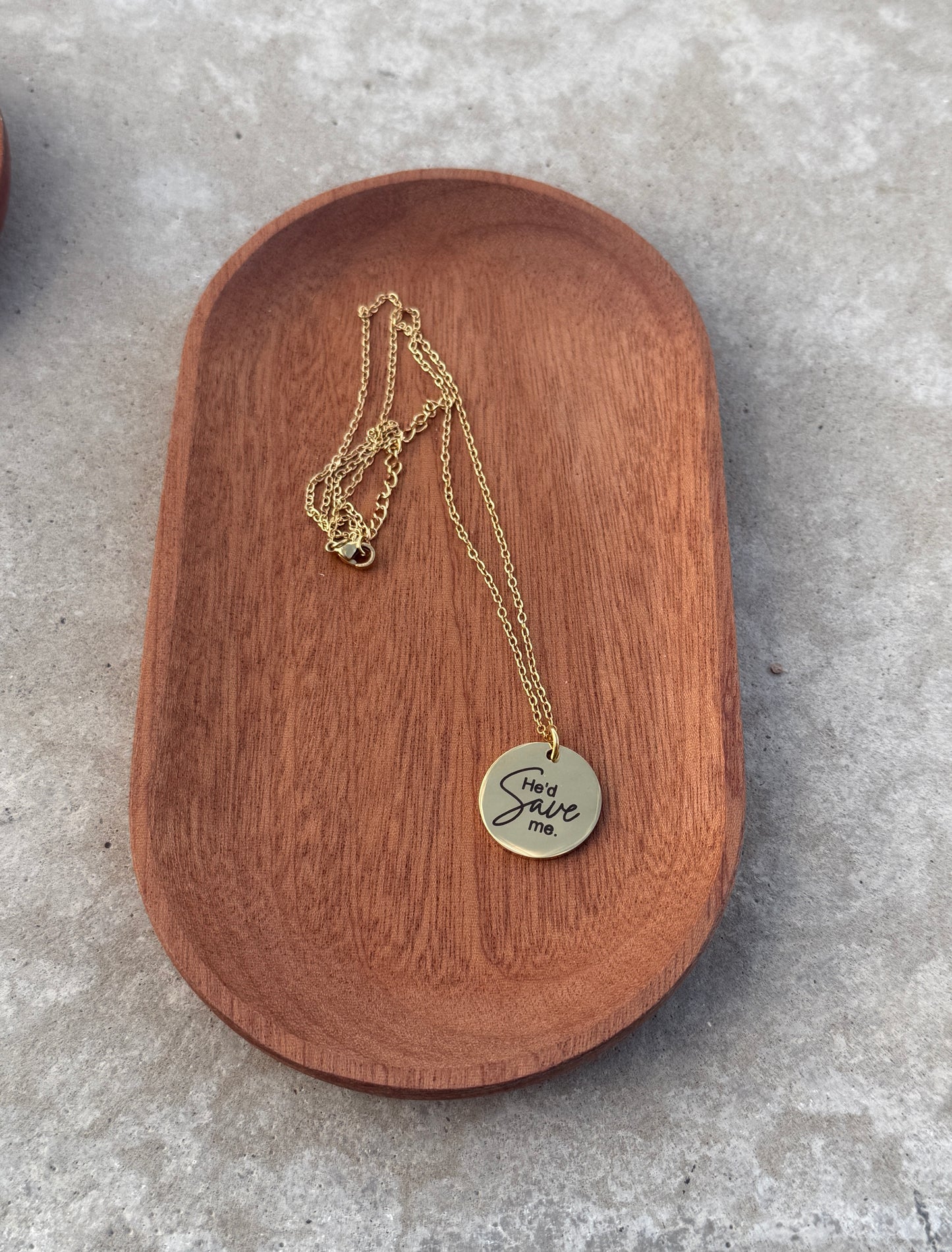 Gold necklace with a round pendant on a wooden dish
