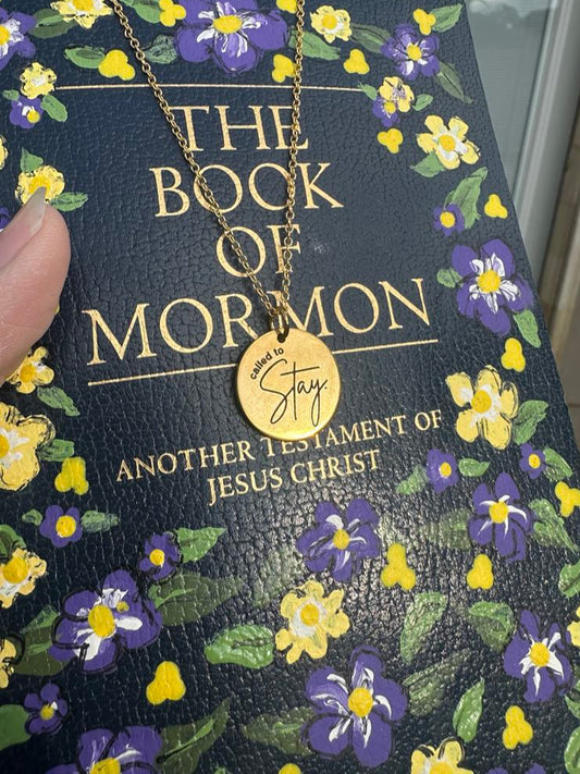 Book of Mormon with floral design and a gold "called to stay" necklace on top