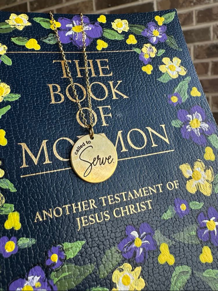 Book of Mormon with floral design and a gold "called to serve" necklace on top