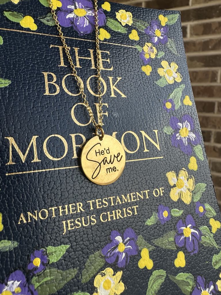 Gold necklace with 'He'd Save Me' pendant on a 'Book of Mormon' with floral design.