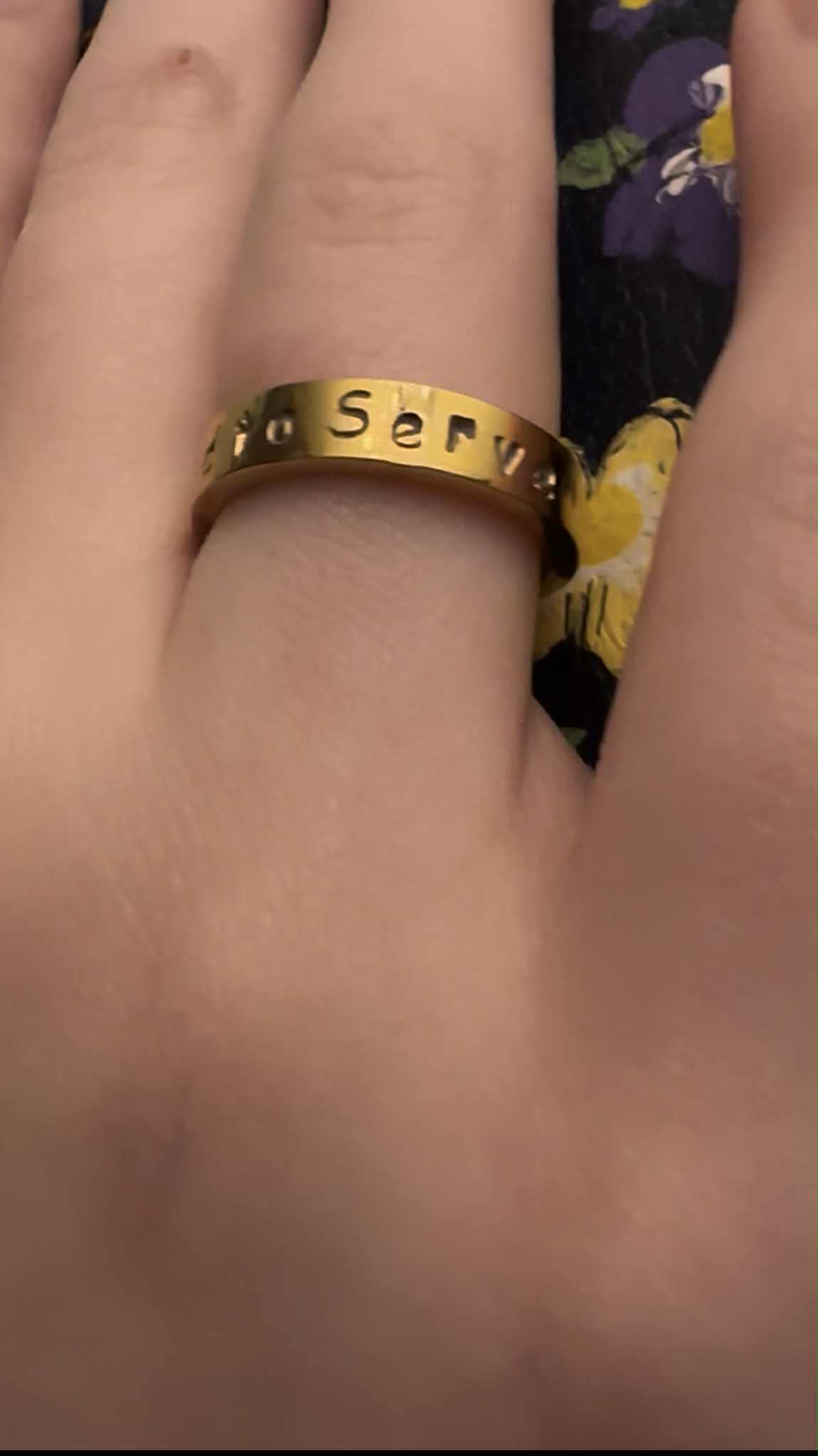 Gold ring with engraved text that says "called to serve" on a finger