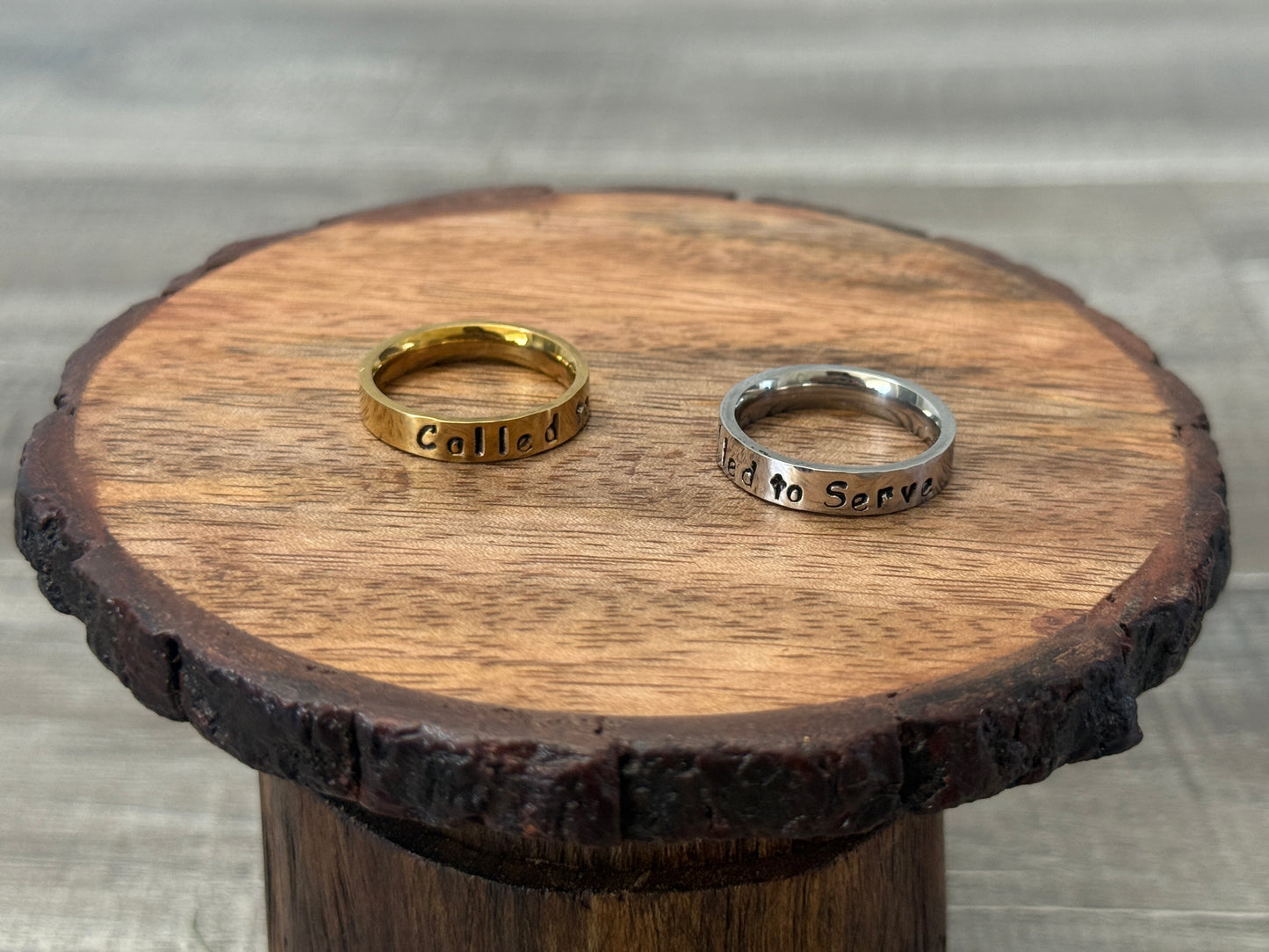 Two called to serve rings, one gold and one silver, on a wooden stand.