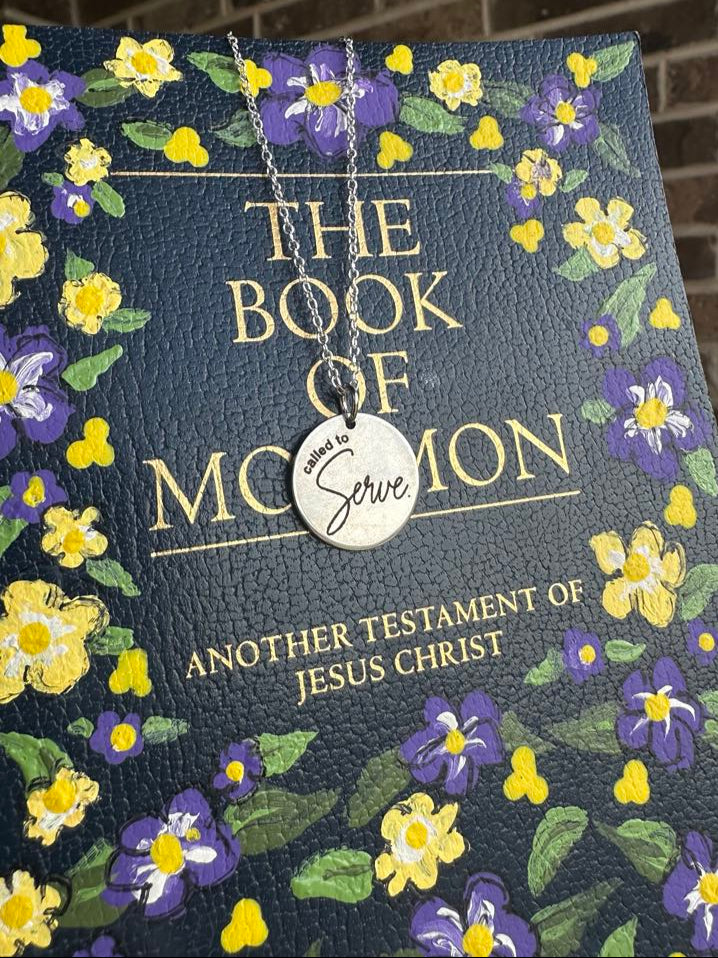 Book of Mormon with floral design and a silver called to serve necklace on top