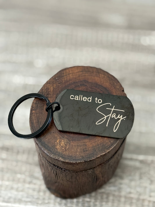 Keychain with 'called to stay' tag on a wooden block against a textured background