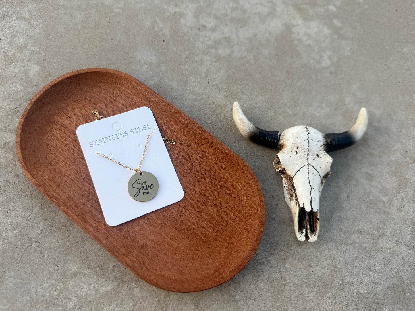 Necklace with pendant on a card next to a cow skull on a concrete surface