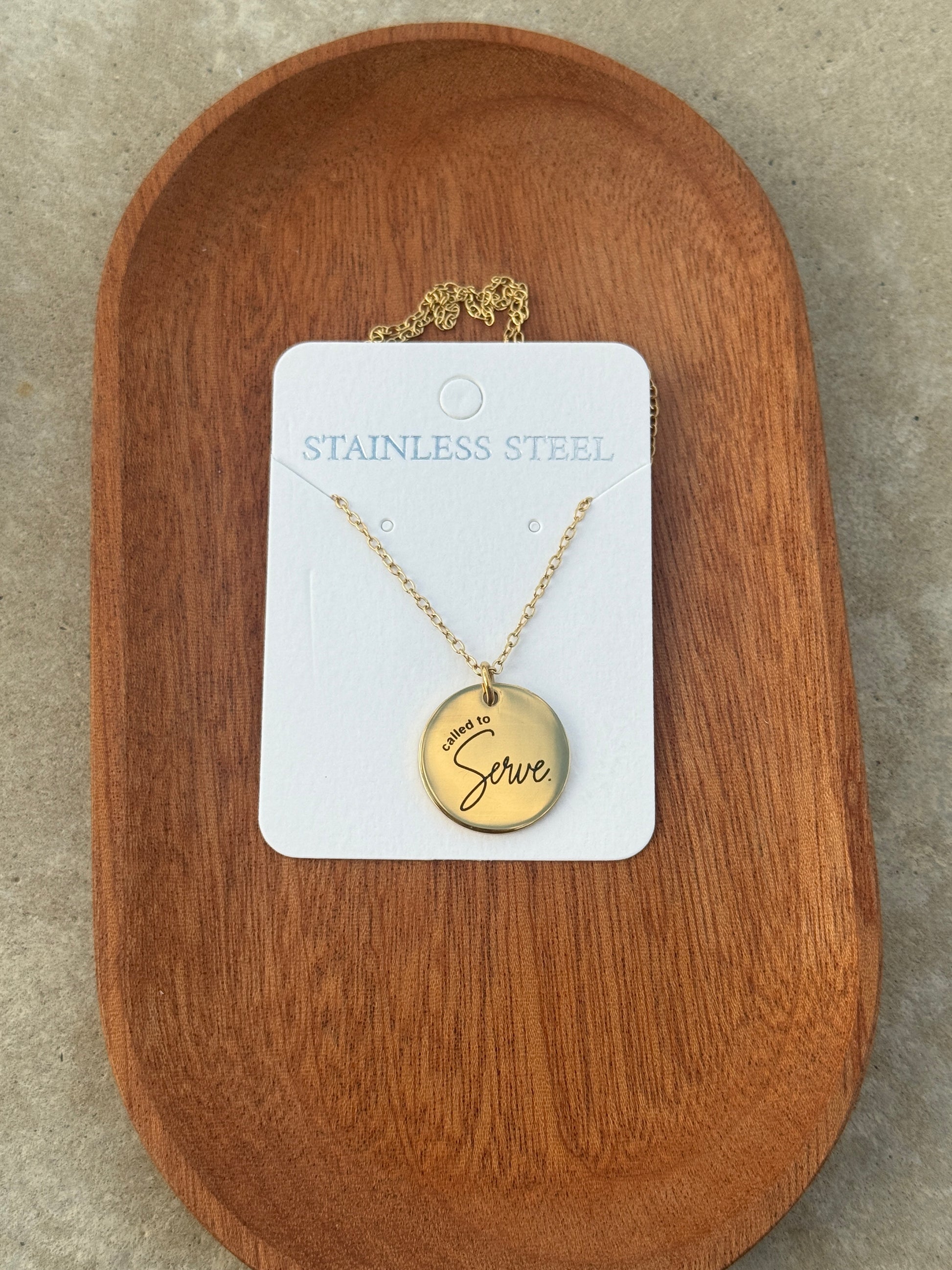 Gold necklace with a pendant on a white card, placed on a wooden surface.