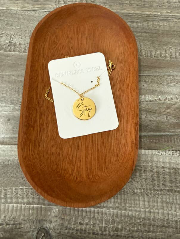 Gold necklace with engraved disc on a white card, placed on a wooden surface.