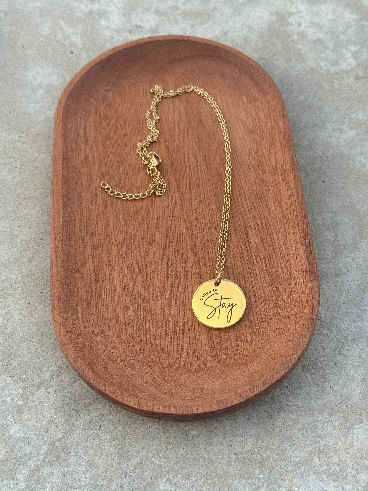 Gold necklace with a round pendant on a wooden tray