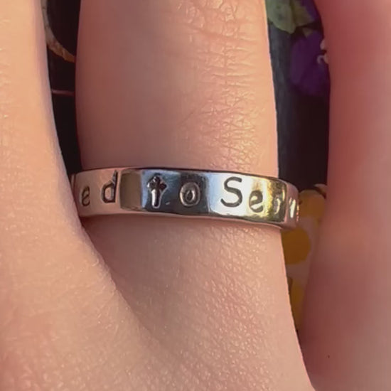silver ring that says called to serve on a finger
