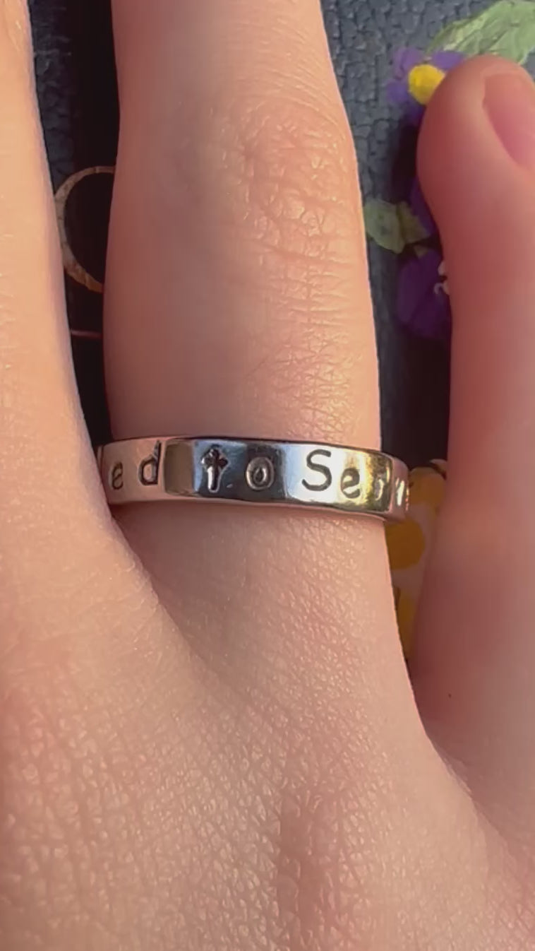 silver ring that says called to serve on a finger

