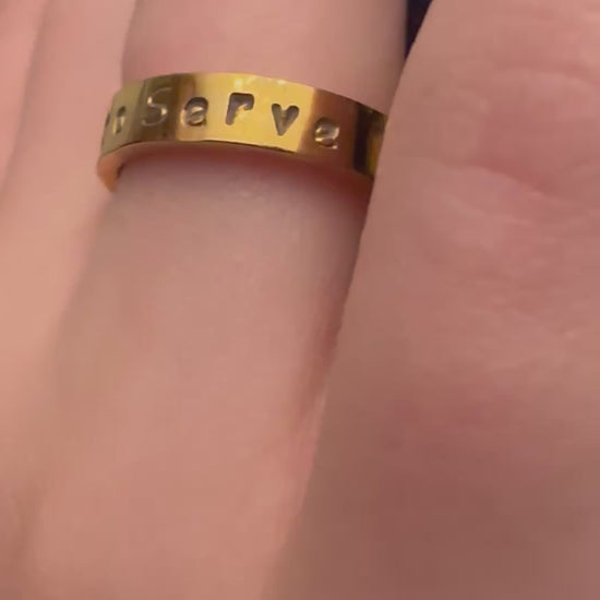 gold ring that says called to serve on a finger
