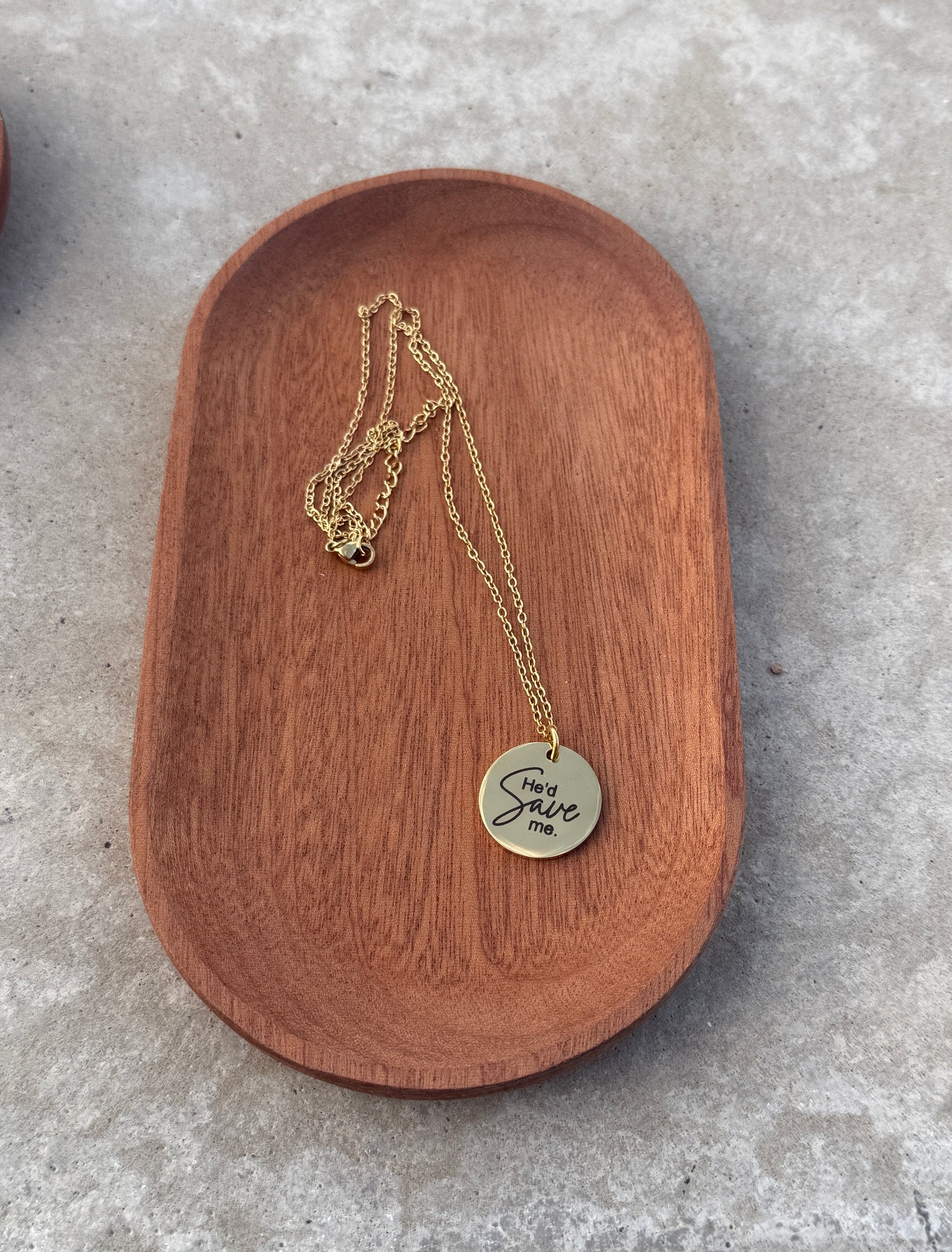 Gold necklace with a round pendant on a wooden dish