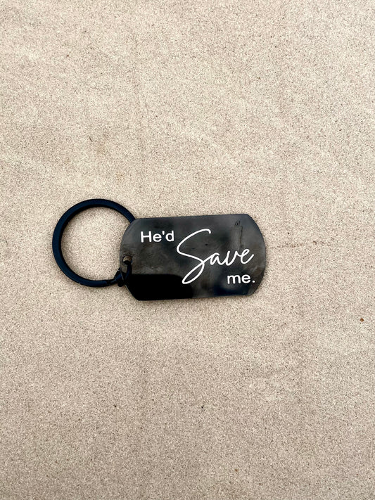 Black keychain with 'He'd Save Me' text on a concrete surface