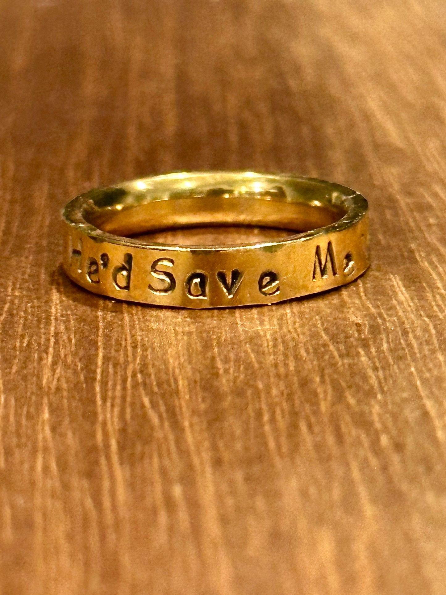 Gold ring that says 'He'd Save Me on a wooden surface