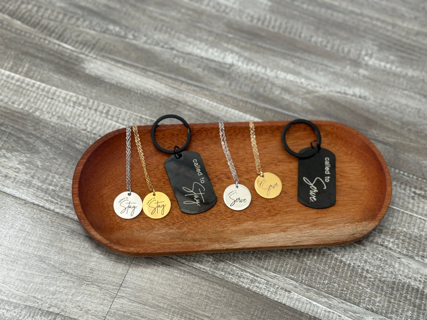 Set of necklaces and keychains on a wooden tray against a gray textured background