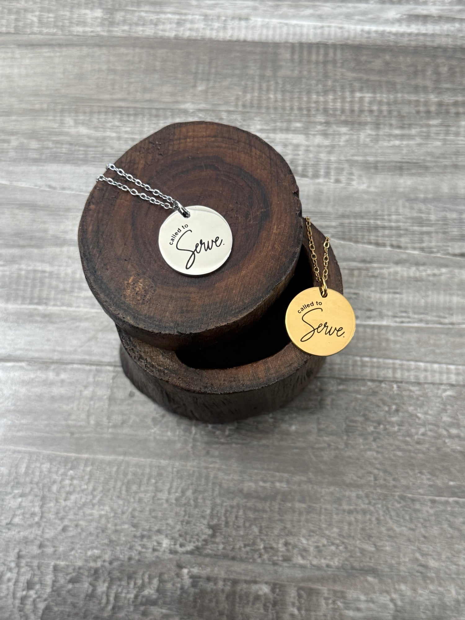 Gold and silver "Called to Serve" necklaces on wooden blocks
