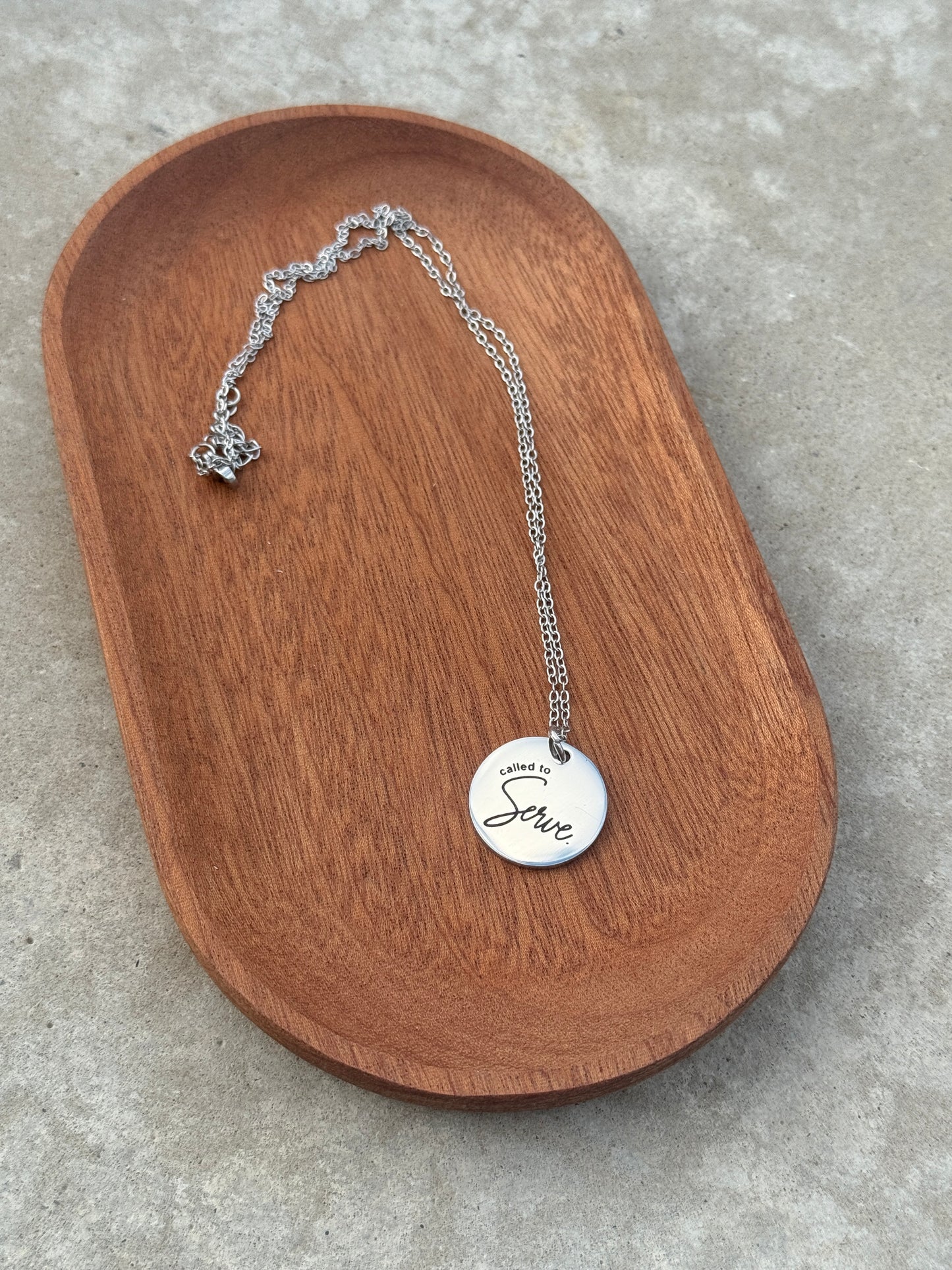 Silver necklace with a round pendant on a wooden tray