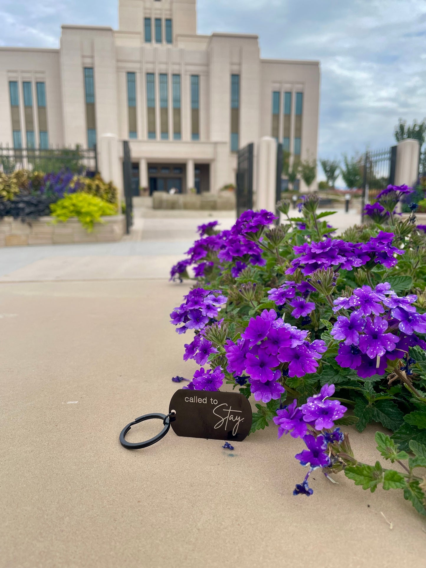 Black 'Called to stay' keychain next to purple flowers with the temple in the background